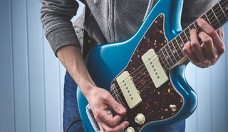 A man plays a blue Fender Jazzmaster