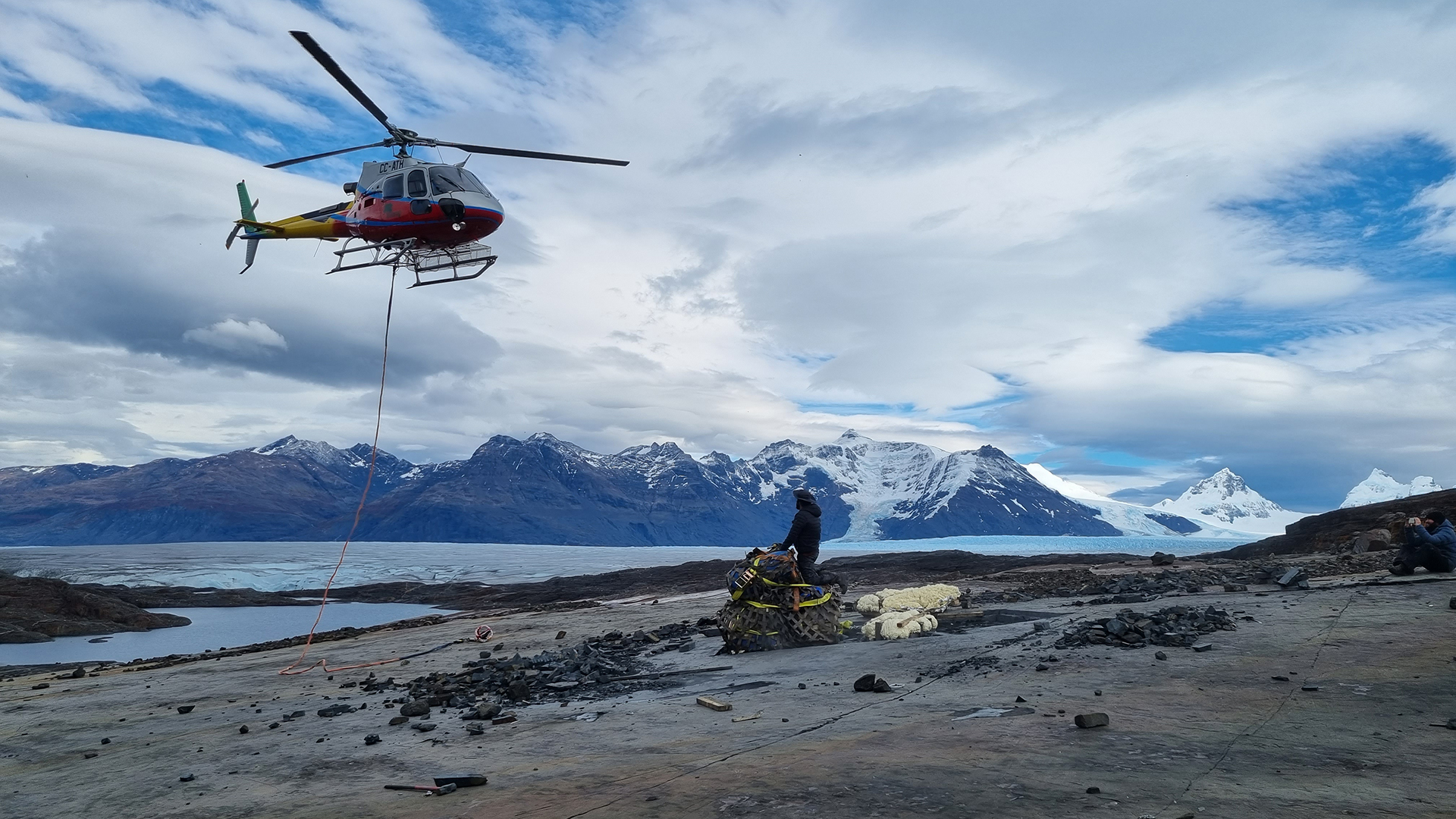 A helicopter prepares to lift the heavy ichthyosaur load, in front of the Tyndall Glacier.