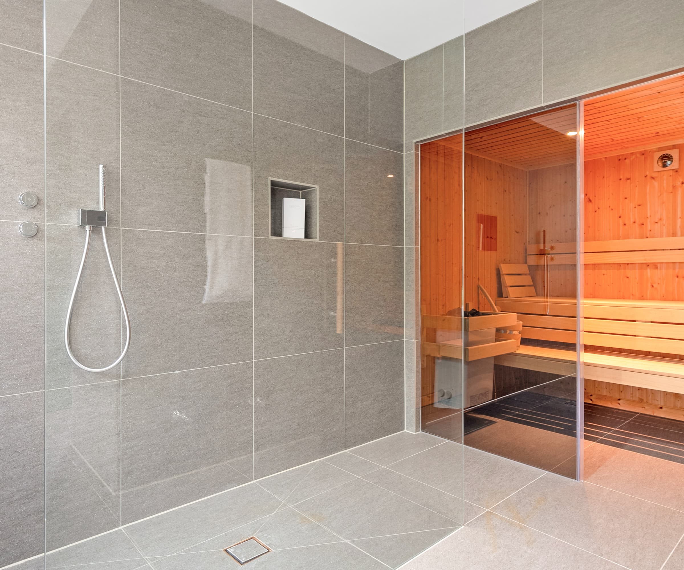 A bathroom with grey tiles and a connecting sauna