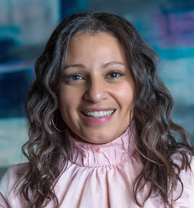 A woman, Dr. Mona Gohara, with wavy hair smiling.