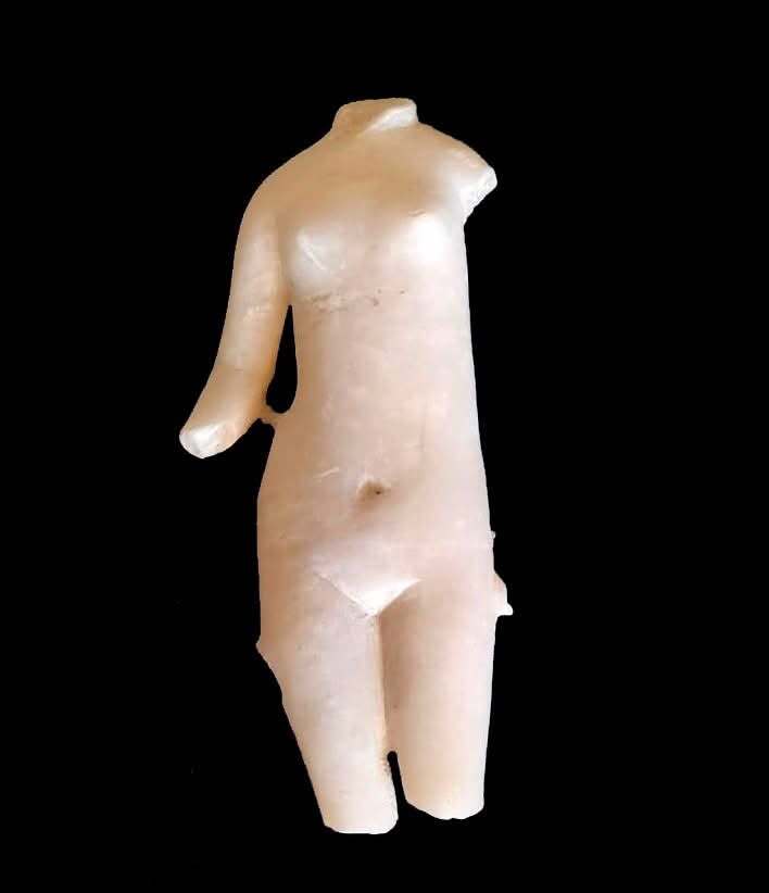 A small white marble statue with one arm stands against a black background.