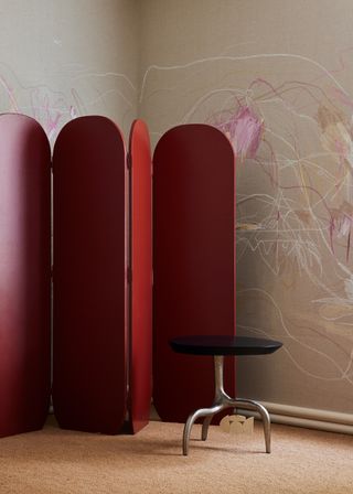 Red room divider with illustrated wallpaper and metal stool on cream floor