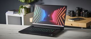 En Razer Blade Pro 17 (2021) står öppnad på ett skrivbord med en mobil och lite kamerautrustning i bakgrunden.