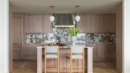 kitchen with marble backsplash and pale wood cabinets and upholstered bar stools