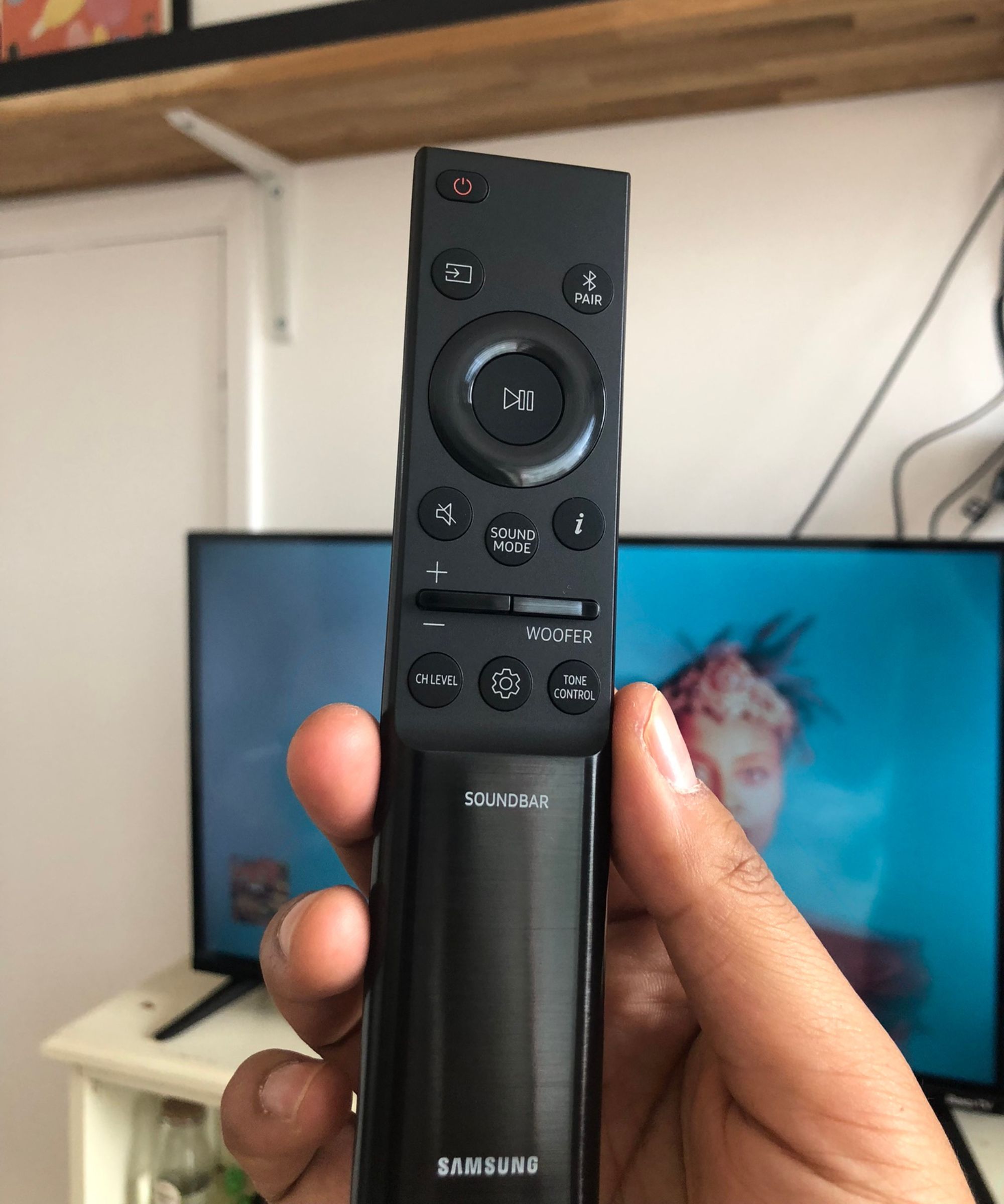 Closeup of Samsung HW-QS750F soundbar remote held in front of TV in Dan Fauzi&#039;s home.