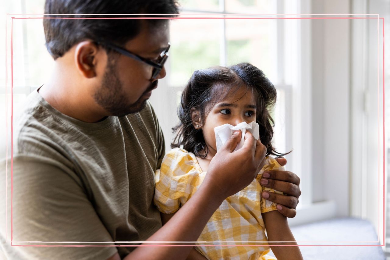 A father wiping his toddler daughter&#039;s nose with a tissue while considering &#039;should I send my child to school with a cold&#039;