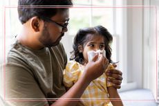 A father wiping his toddler daughter's nose with a tissue while considering 'should I send my child to school with a cold'