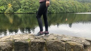 A hikers legs as they stand on a wall next to a river