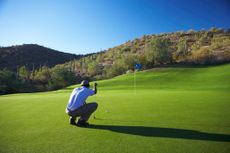 Male golfer lining up putt on golf course