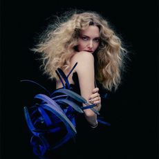 Amanda Seyfried stands looking over her shoulder. She is wearing a black strapless dress with blue feather detailing on the sides.