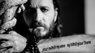 a portrait of kobi garhi holding his tattooed arm up to the camera