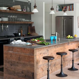 reclaimed wood island with black stools and grey tiled walls