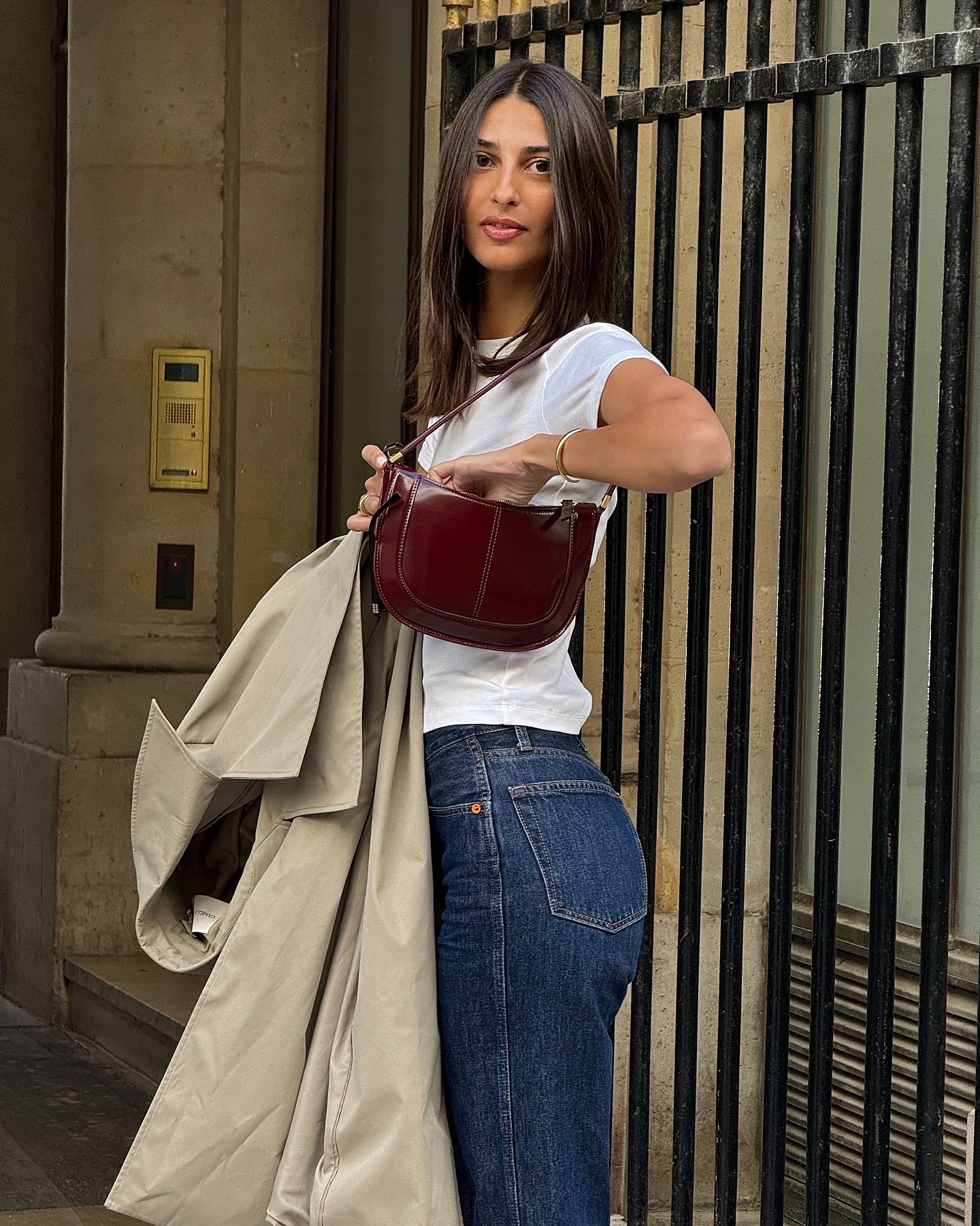 A woman wearing a white t-shirt and jeans getting something out of a dark red handbag with face-framing layers