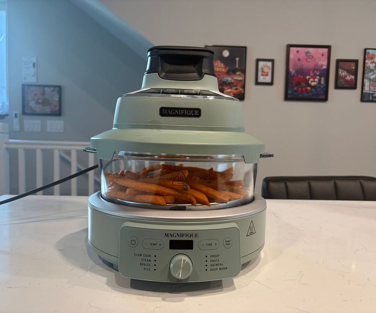 A glass air fryer with a green base on a white countertop filled with sweet potato fries.
