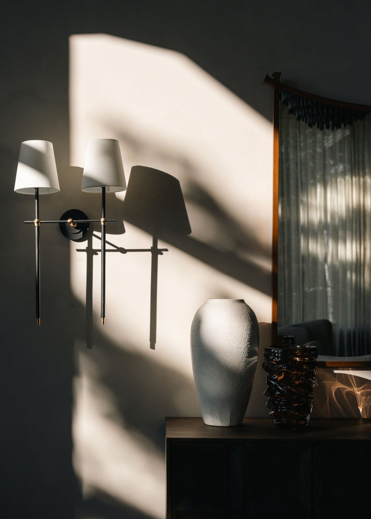 A close-up of a wall sconce and a vase corner in a living room with dappled light