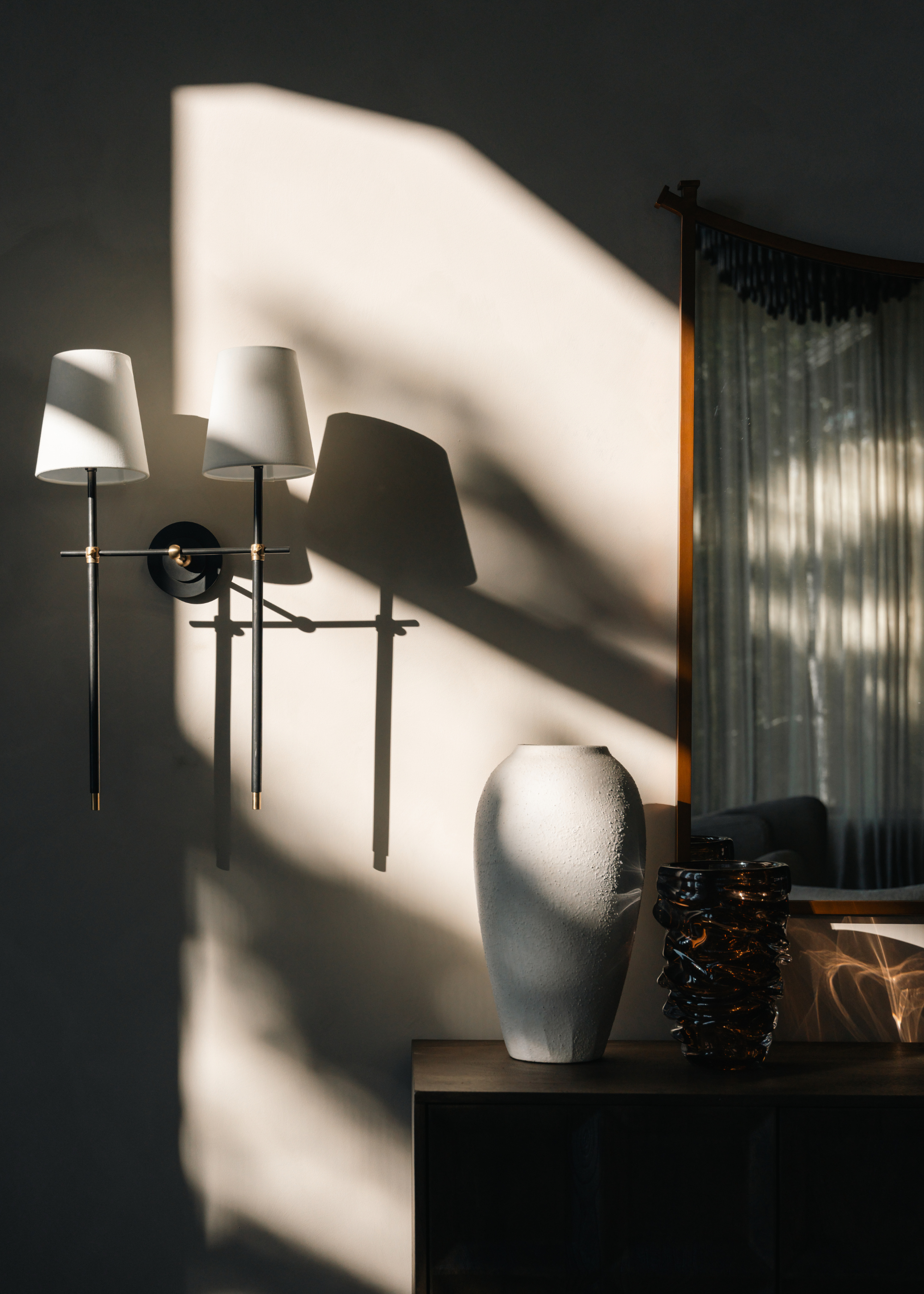 A close-up of a wall sconce and a vase corner in a living room with dappled light
