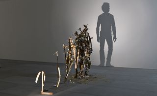 A closer view of one shadow sculpture made out of junk, metal, and wood. The light shines on the sculpture and casts a shadow on the wall. The shadow portrays a man looking into the distance.