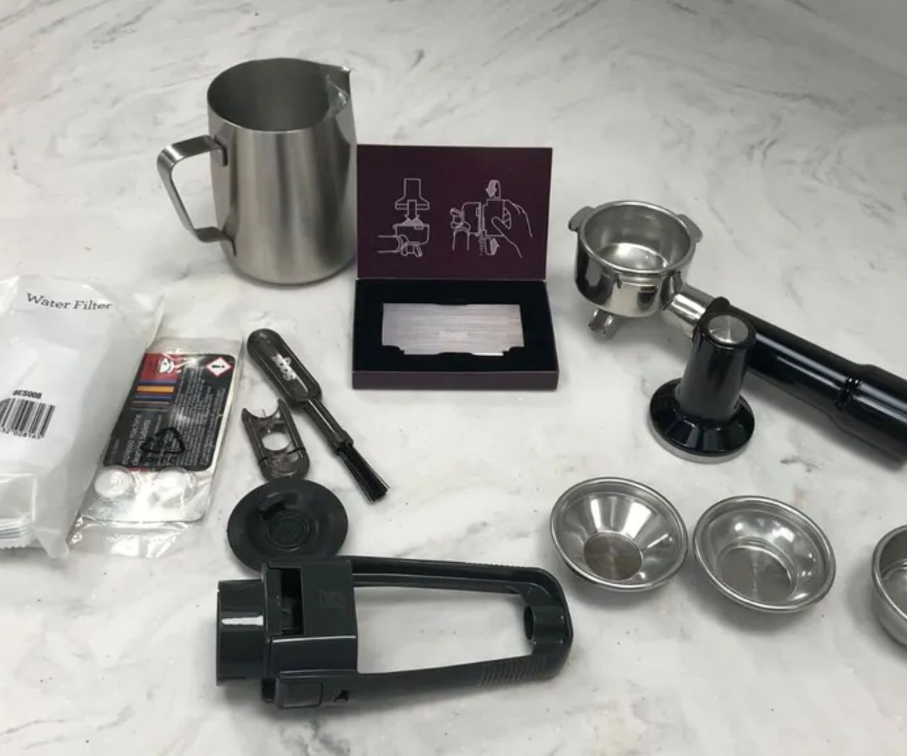 the accessories for the Breville Barista pro laid out on a marble counter,