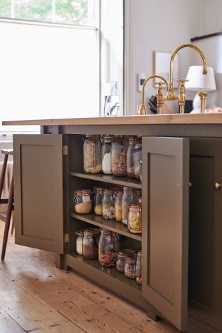 an open sage green kitchen cabinet filled with decanted pantry supplies