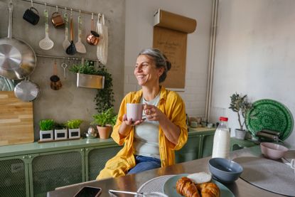 Photo of a woman having a first morning coffee in the kitchen of her apartment.