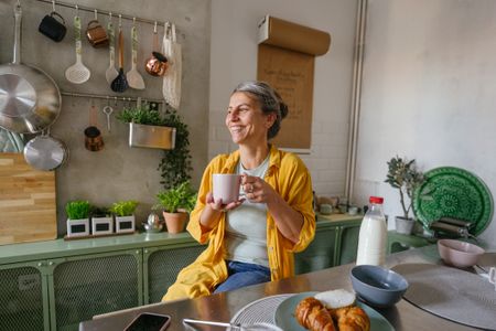 Photo of a woman having a first morning coffee in the kitchen of her apartment.