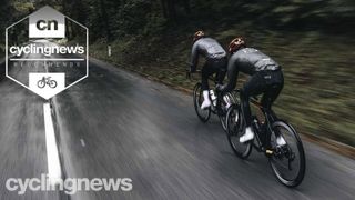 Two road cyclists riding along a wet-looking road in winter cycling kit