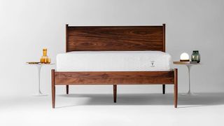 A face on shot of the Tiami Mattress on a wooden bed frame in a white room, two small tables are placed either side of the bed
