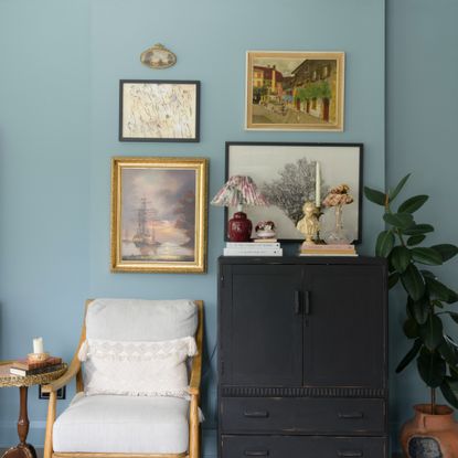A blue-painted living room with a small gallery wall and an antique black cabinet
