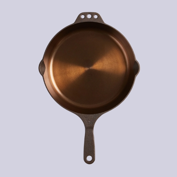 A brass-coated, cast-iron pan against a lilac background.