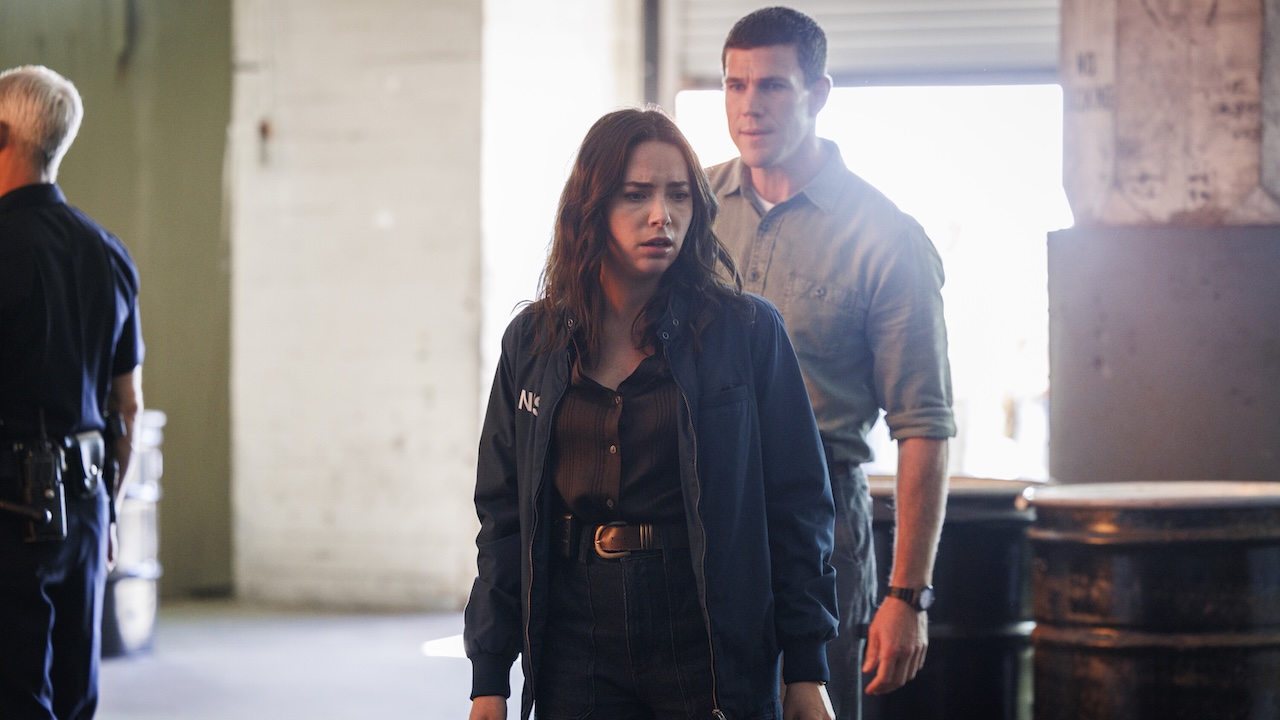 Lala looking down at her CI being treated by paramedics while Gibbs stands behind her in NCIS: Origins