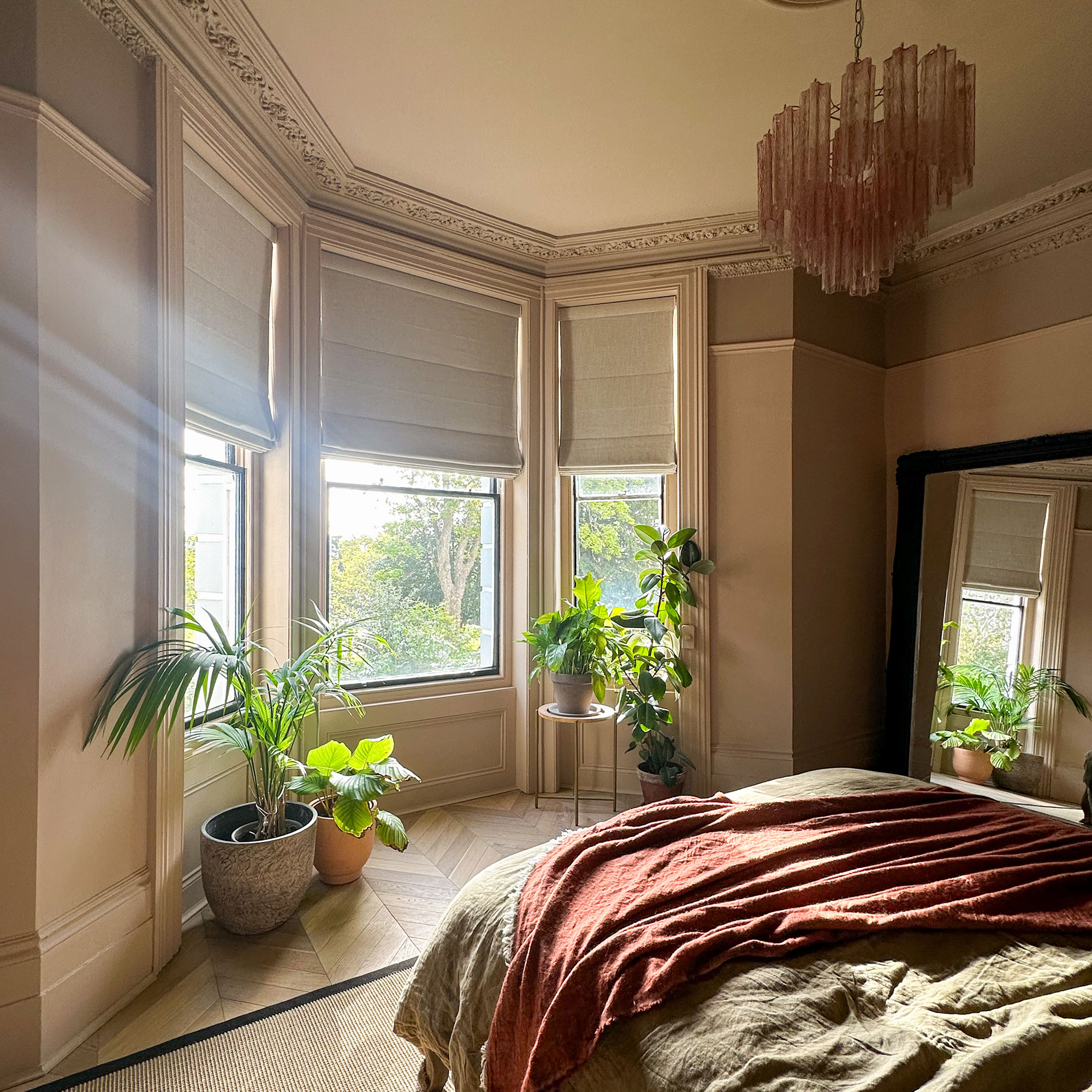 Neutral bedroom with chandelier, linen bedding and bay window area with houseplants
