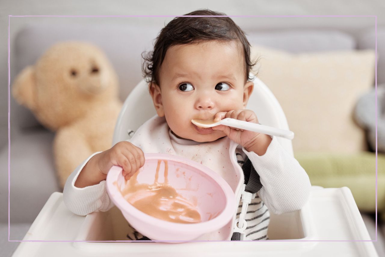 A baby with a sponnin their mouth holding onto a bowl