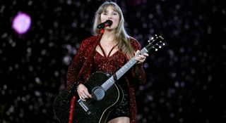 Taylor Swift wears a red sequinned top and plays a black spark Gibson J-45 acoustic guitar live onstage in Vancouver as her record-breaking Eras Tour comes to a close.