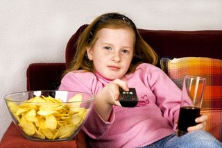 A young girl watches television and eats junk food.
