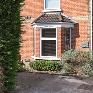 Concrete and block paving driveway outside brick house with evergreen hedge in foreground