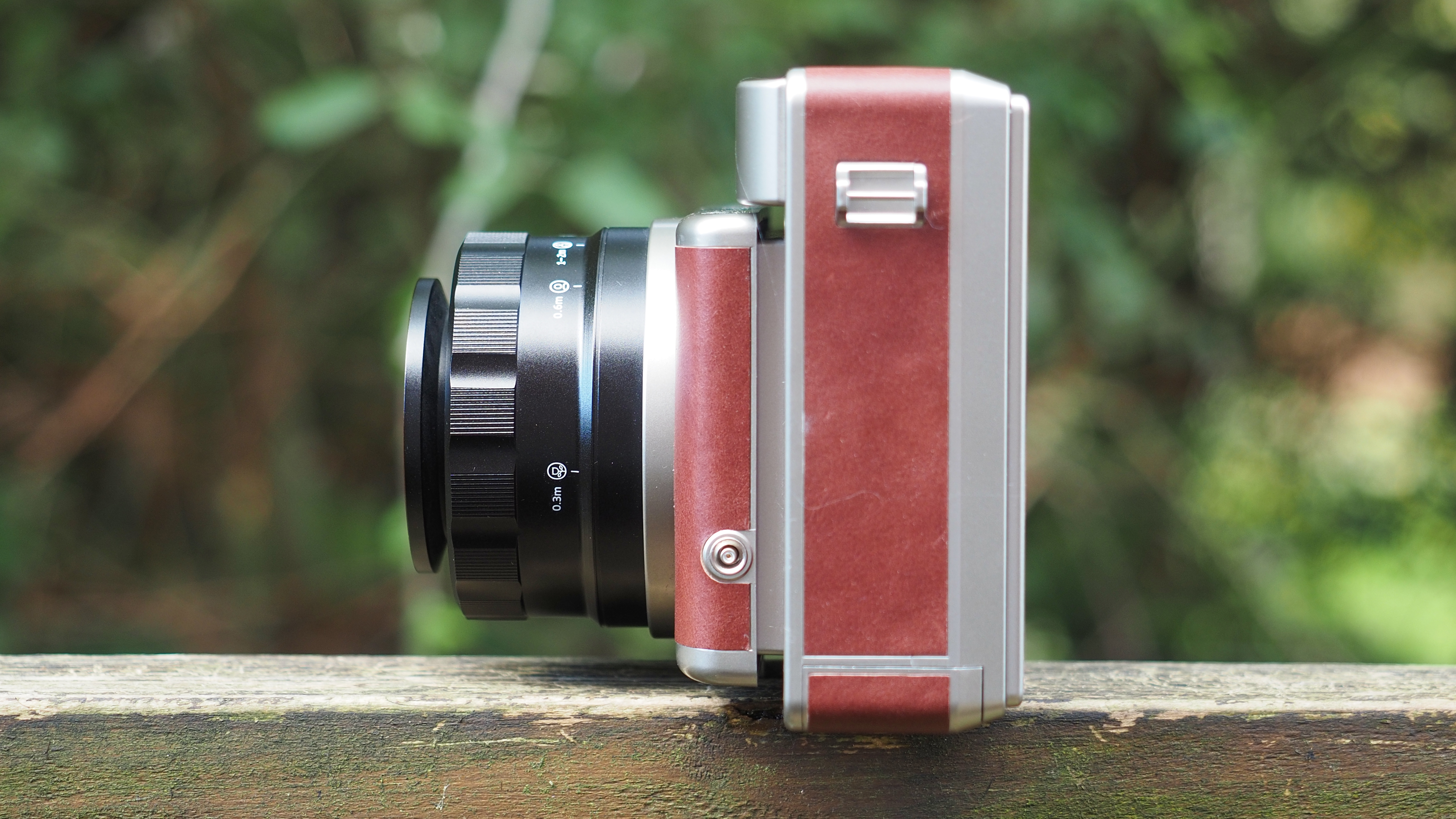 Lomo'Instant Wide Glass camera, sitting on a wooden surface, outdoors against a wooded background