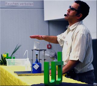 Dr. Cary Supalo presents to an organization in Dortmund Germany information about how to make science activities accessible to the blind. He is demonstrating a safe technique for determining if a Bunsen burner is on and water is boiling.