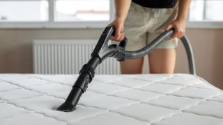 Woman wearing beige shorts while vacuuming her white mattress 