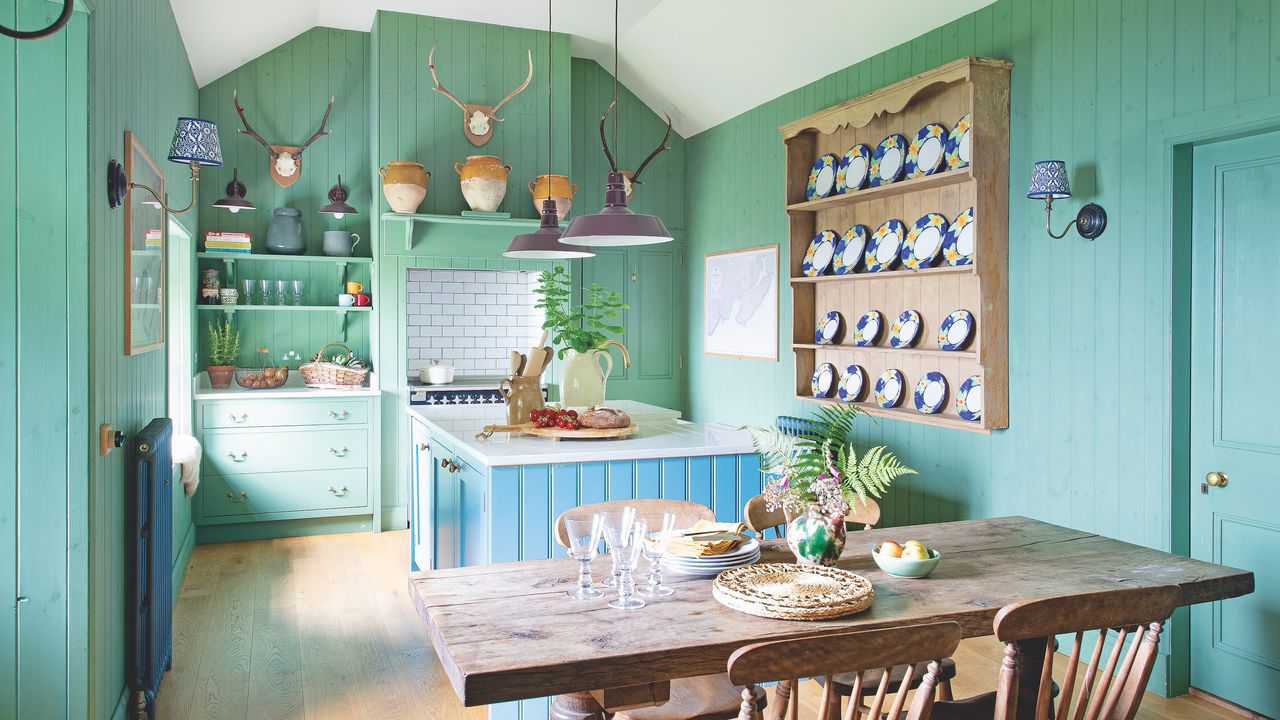 cottage kitchen with green walls and base units, blue island, open shelves and farmhouse table