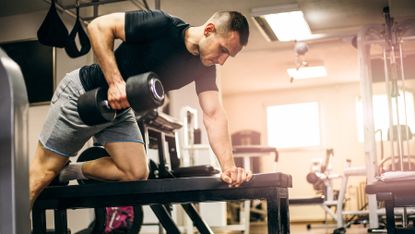 Man performing a dumbbell row over a bench at the gym