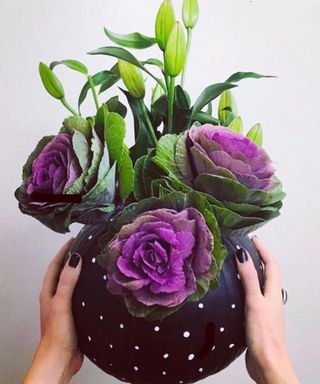 DIY pumpkin vase idea with black paint and white dot motif, with cabbage flowers held against white wall decor