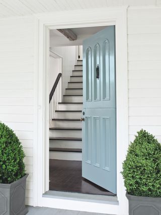 Light blue front door on house with white siding open to hall and staircase