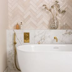 White free standing bath with pink herringbone tiles, a marble back splash