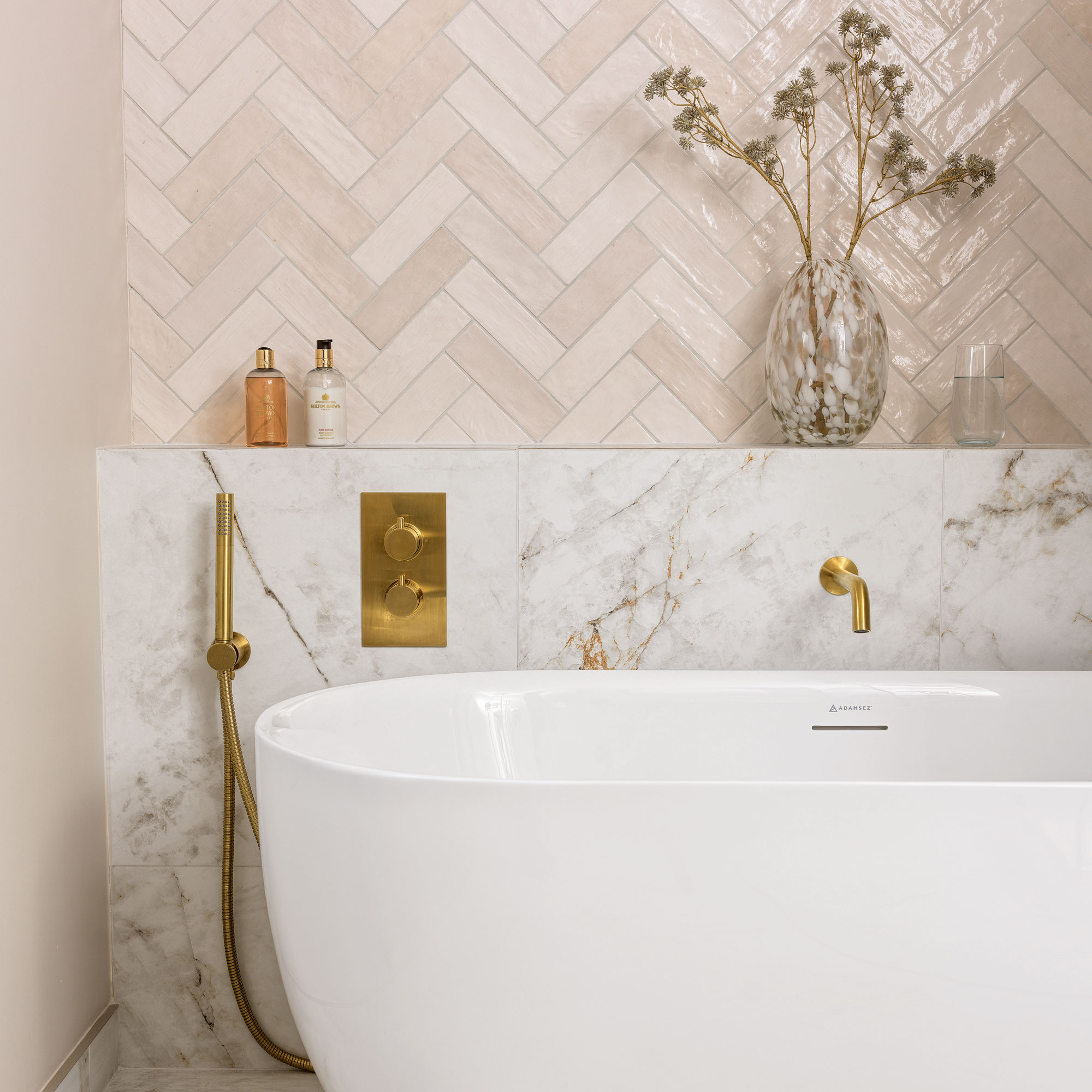 White free standing bath with pink herringbone tiles, a marble back splash