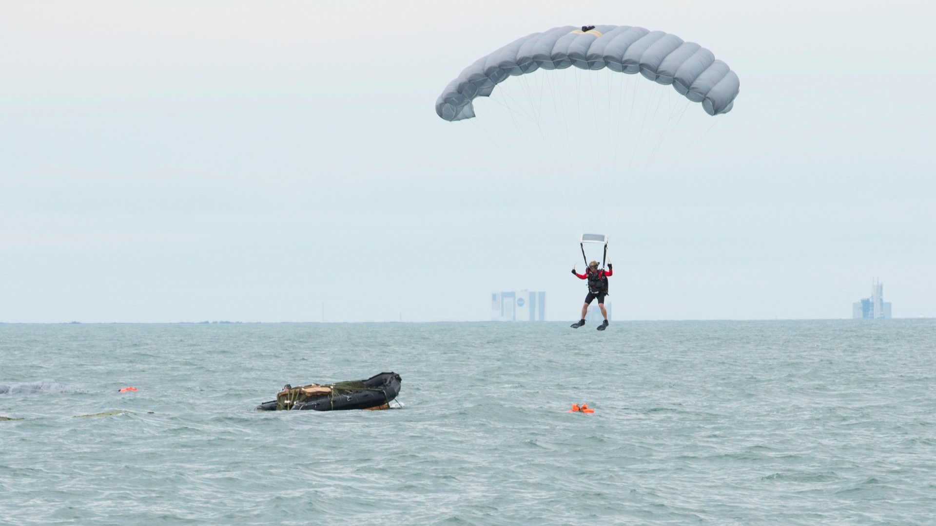 a person wearing flippers and a helmet descends into the ocean under a parachute next to an inflatable boat