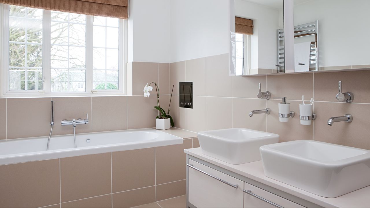 Clean, pink bathroom with bath, sink and light entering from window - for article on all the places you&#039;re probably forgetting to clean in your bathroom