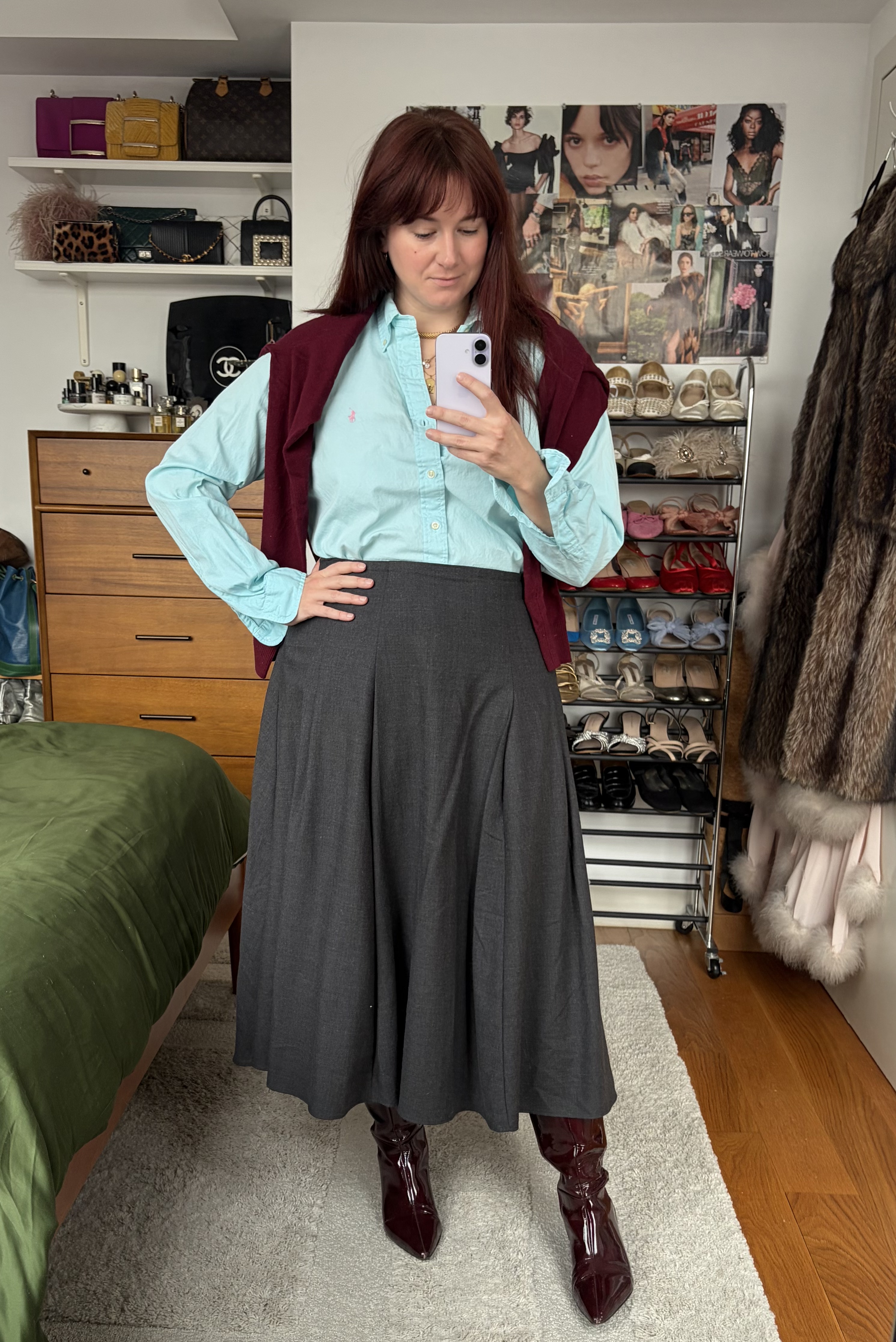 Tyler McCall wearing J.Crew's red mens cashmere sweater over her shoulders, a blue button-down shirt, gray pleated skirt, and red leather tall boots
