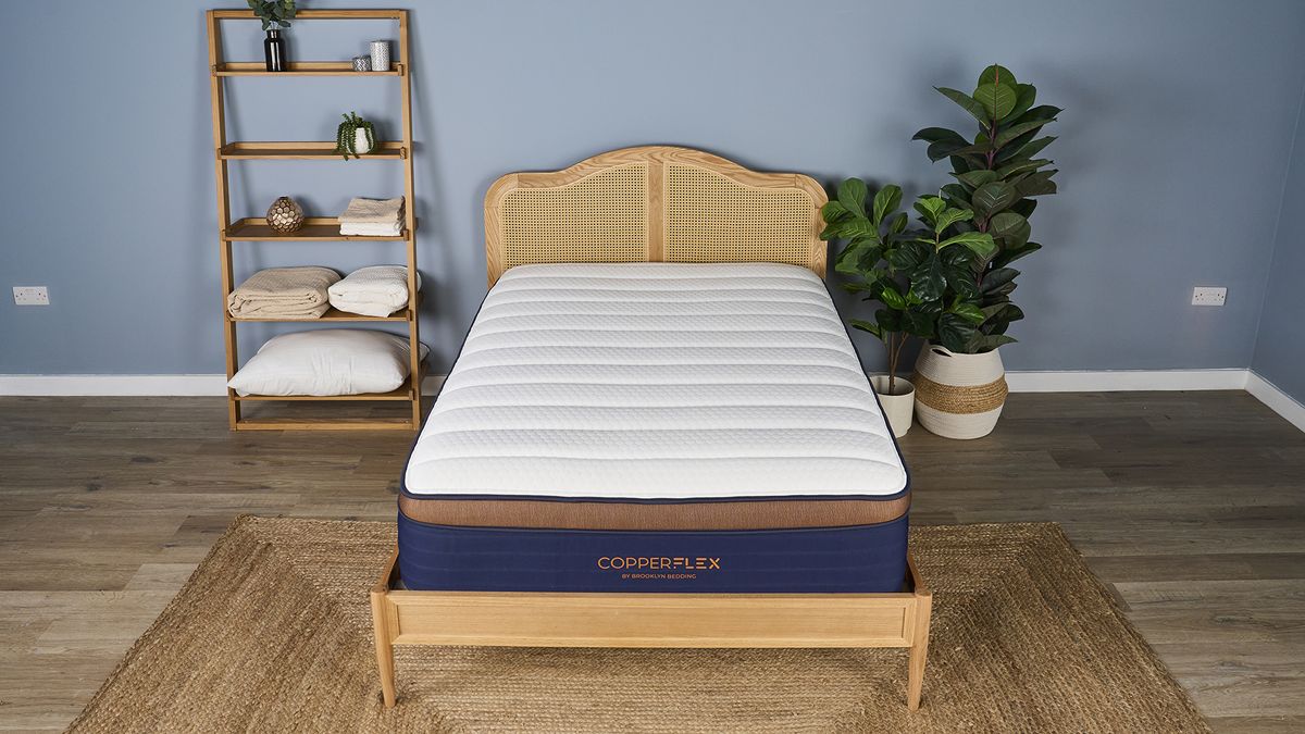 White, navy and bronze Brooklyn Bedding CopperFlex Pro Hybrid Mattress on rattan bedframe in sleep studio with shelves and plants