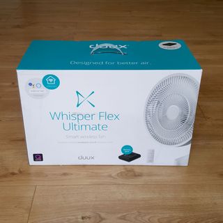 The white Duux Whisper Flex Ultimate Fan in its packaging on a wooden floor