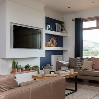 A living room with two leather brown sofas facing each other and a TV hanging on the wall in the middle